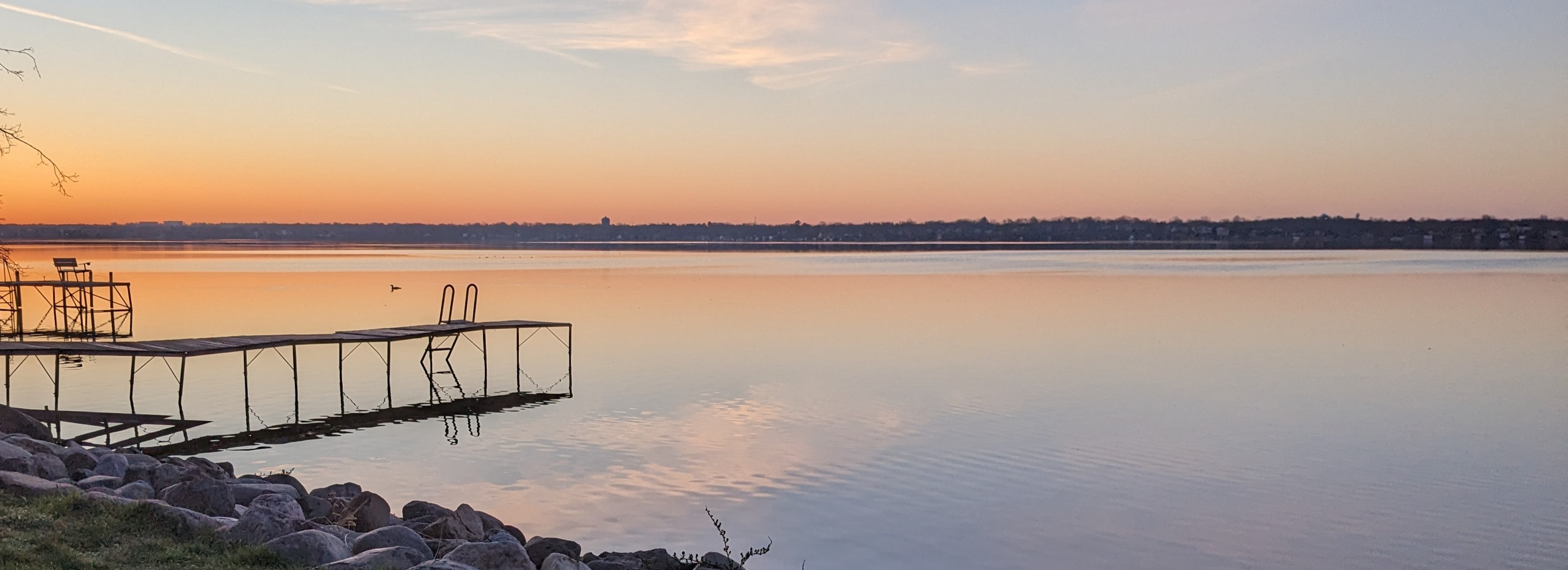 image of lake Monona at sunrise. the lake is still and a dock can be seen at the lower left